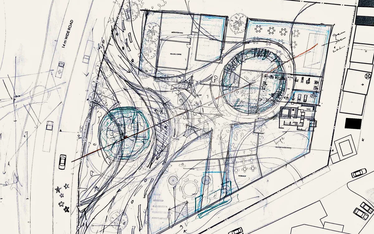 Pencil and blue-pencil iteration over the printed site plan: two circular courts joined by sweeping curved paths that bridge from the road into the site.